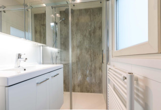 Moderne badkamer met glazen douche, wit wastafelmeubel en raam in Lodge Module II in Nederland.