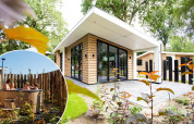Alojamiento glamping moderno con fachada de madera, grandes ventanales y jacuzzi exterior privado.