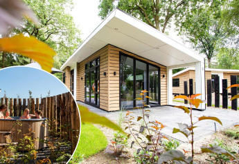 Hébergement glamping moderne avec façade en bois, grandes baies vitrées et bain à remous extérieur.