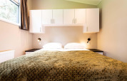 Chambre de lodge avec un grand lit, placards blancs au-dessus, couvertures vertes et lampe murale.