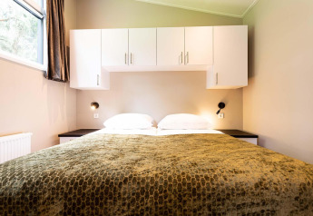 Lodge-slaapkamer met tweepersoonsbed, witte kasten boven het bed, groene deken en nachtlampen.