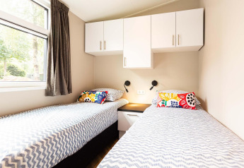 Luminoso dormitorio de lodge con dos camas individuales, cojines coloridos y armarios encima de las camas.