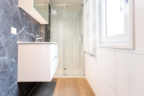 Baño moderno en una posada con cabina de ducha de vidrio, lavabo elegante y ventana grande luminosa.