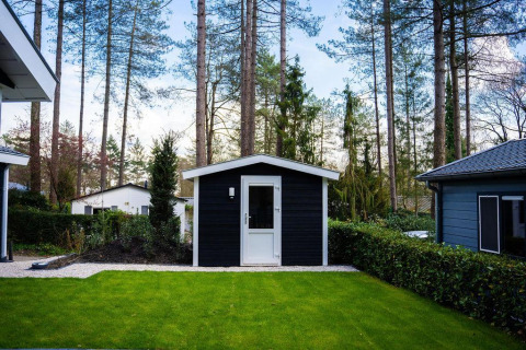 Césped verde y pequeño cobertizo negro en una cabaña boscosa, Heuvelrug Cottage, De Thijmse Berg, Países Bajos.