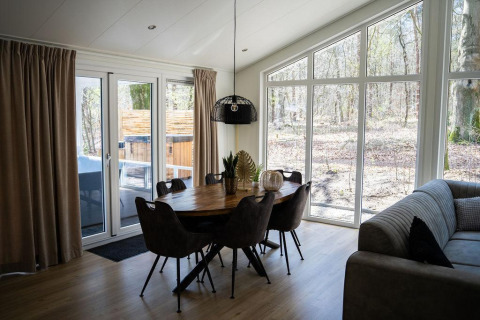 Comedor con grandes ventanales y vista al bosque en Heuvelrug Cottage con jacuzzi en De Thijmse Berg, Países Bajos.