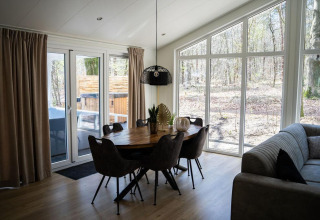 Comedor con grandes ventanales y vista al bosque en Heuvelrug Cottage con jacuzzi en De Thijmse Berg, Países Bajos.