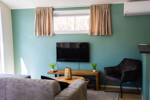 Sala moderna en Heuvelrug Cottage con sofá, TV, pared turquesa y ventana en De Thijmse Berg, Países Bajos.