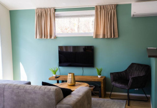 Sala moderna en Heuvelrug Cottage con sofá, TV, pared turquesa y ventana en De Thijmse Berg, Países Bajos.