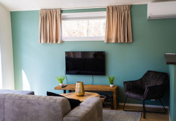 Modern living room at Heuvelrug Cottage with teal walls, TV, sofa, armchair, and window at De Thijmse Berg.