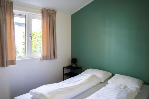 Dormitorio luminoso en Heuvelrug Cottage en De Thijmse Berg, Países Bajos, con pared verde y dos camas.