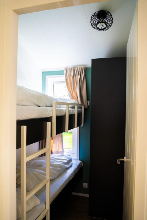 Schmales Zimmer mit Etagenbett, Schrank und Fenster im Heuvelrug Cottage + Whirlpool bei De Thijmse Berg, Niederlande.