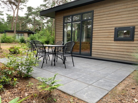 Außenterrasse eines kleinen Waldchalets im Ferienpark De Kleine Belties, Niederlande, mit Sitzbereich.