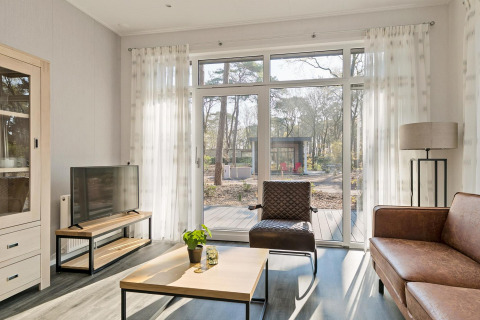 Lyst opholdsområde i Forest park chalet ved De Kleine Belties feriepark, med udsigt til skov i Holland.