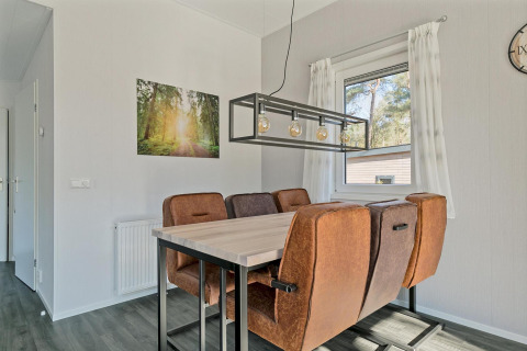 Eethoek in Forest park chalet met bruine stoelen, moderne lampen en uitzicht op bos bij De Kleine Belties, Nederland.