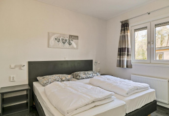 Soveværelse i Forest park chalet ved De Kleine Belties, med dobbeltseng, natborde og store vinduer.