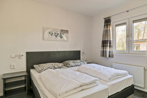 Slaapkamer in Forest park chalet bij vakantiepark De Kleine Belties, met tweepersoonsbed en grote ramen.