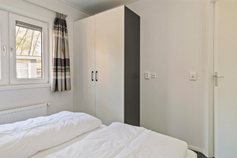 Lichte slaapkamer in Forest park chalet bij Holiday park De Kleine Belties met kast en raam.