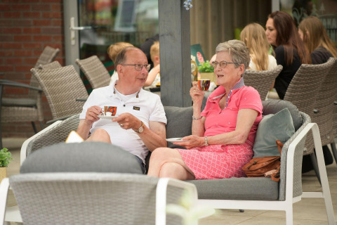 Ouder koppel geniet van koffie op een terras bij een glampingverblijf, omringd door andere gasten.