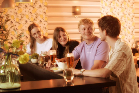 A group of young adults enjoying drinks and conversation at a bar inside a glamping accommodation setting.