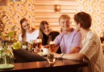 En gruppe unge voksne hygger sig sammen ved en bar på en glamping-indkvartering med drinks og mad.