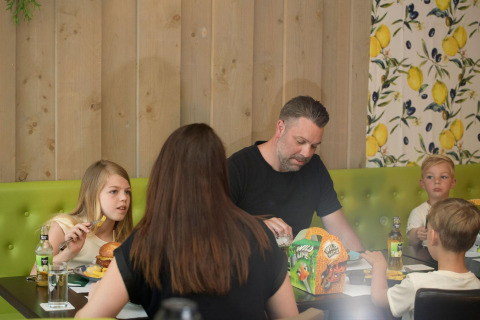 Een gezin van vier zit samen te eten aan een tafel in een glampingverblijf met groene zitbank.