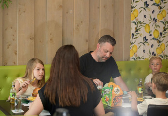 Une famille de quatre personnes partage un repas à une table dans un hébergement glamping, banquette verte.
