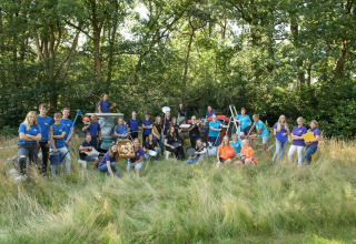 Equipo numeroso posando en un alojamiento glamping, rodeados de utensilios y naturaleza al aire libre.