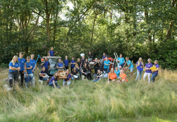 Stort team poserer udendørs ved glamping, omgivet af udstyr og natur, klar til at byde gæster velkommen.