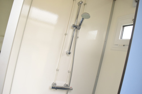 Modern shower setup inside the Safari cottage at Holiday park De Boshoek in the Netherlands, white wall.
