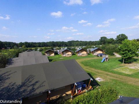 Tentes safari au parc de vacances De Boshoek aux Pays-Bas, sur une pelouse verte avec une aire de jeux et ciel bleu.