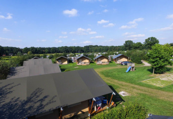 Safaritenten op vakantiepark De Boshoek in Nederland met grote grasvelden en speeltuin onder blauwe lucht.