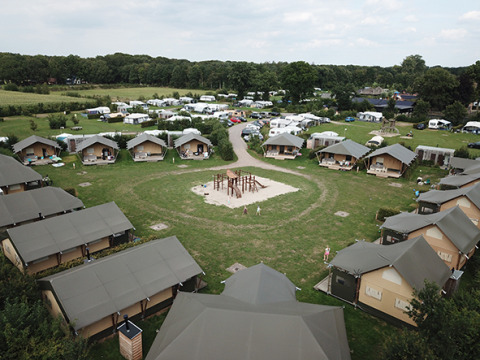 Vista aérea de un camping con tiendas safari, caravanas y área de juegos infantil en el centro del campo.