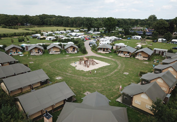 Luchtfoto van safaritenten op een camping met caravans en een speeltuin in het grasveld centraal gelegen.