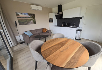 Sala moderna de lodge en los Países Bajos con mesa redonda, cocina, sofá y obra de arte en la pared.