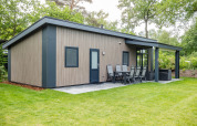 Forest Lodge DeLuxe en Kampeerdorp de Zandstuve, moderna cabaña de madera con terraza en entorno natural verde.