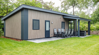 Forest Lodge DeLuxe en Kampeerdorp de Zandstuve, moderna cabaña de madera con terraza en entorno natural verde.