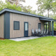 Forest Lodge DeLuxe en Kampeerdorp de Zandstuve, moderna cabaña de madera con terraza en entorno natural verde.