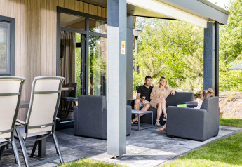 Familie sidder sammen på terrassen af Forest Lodge DeLuxe ved Kampeerdorp de Zandstuve, Holland.