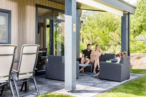 Familie sidder sammen på terrassen af Forest Lodge DeLuxe ved Kampeerdorp de Zandstuve, Holland.