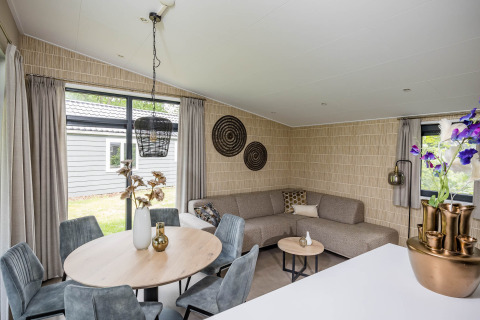 Modernes Wohnzimmer im Forest Lodge DeLuxe in Kampeerdorp de Zandstuve mit gemütlichem Sofa und Esstisch.