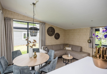 Moderne opholdsstue i Forest Lodge DeLuxe på Kampeerdorp de Zandstuve, indrettet med komfortabel sofa og spisebord.