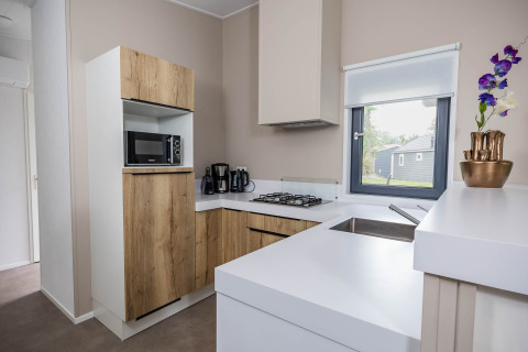 Cocina moderna en Forest Lodge DeLuxe con armarios de madera, microondas y ventana en Kampeerdorp de Zandstuve.