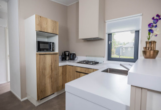Cocina moderna en Forest Lodge DeLuxe con armarios de madera, microondas y ventana en Kampeerdorp de Zandstuve.