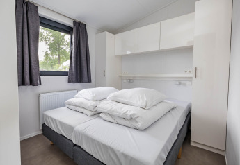 Slaapkamer met tweepersoonsbed, witte kasten en raam in Forest Lodge DeLuxe, Kampeerdorp de Zandstuve.