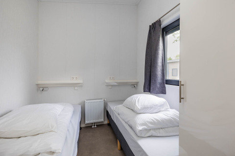 Bedroom with two single beds, white bedding, a large window, and grey curtains at Forest Lodge DeLuxe.