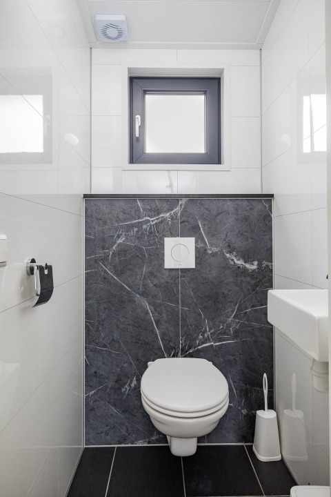 Moderne toilet på Forest Lodge DeLuxe i Kampeerdorp de Zandstuve, Holland, med grå og hvide fliser.