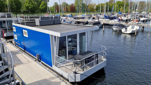 Moderne blå husbåd Havenlodge N fortøjet ved Marina Parcs Naarden i Holland med lystbåde i baggrunden.
