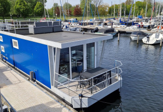 Moderne blauwe woonboot Havenlodge N aangemeerd bij Marina Parcs Naarden in Nederland, met jachten vlakbij.