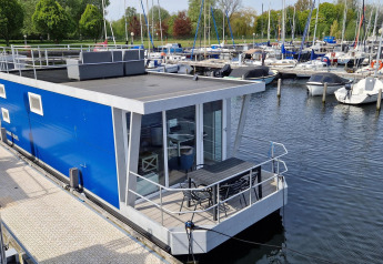 Moderne péniche bleue Havenlodge N amarrée à Marina Parcs Naarden aux Pays-Bas avec des bateaux autour.