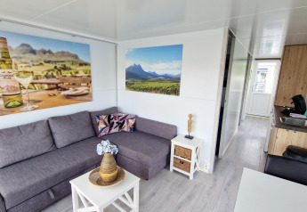 Sala de estar en una casa flotante en Havenlodge N de Marina Parcs Naarden, con sofá gris y arte mural.